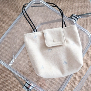 Detail of cream canvas tote showing blue bow embroidery and secure snap button closure