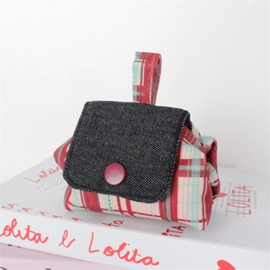 Close-up of cute plaid canvas mini pouch with denim flap and red button on white books