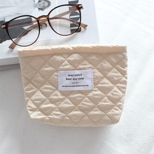 Detailed close-up of a quilted cream cosmetic bag with a minimalist woven brand label