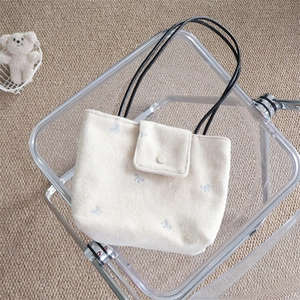 Detail of beige tote bag featuring blue bow embroidery and black handles on a chair