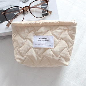 Close-up of cream quilted cosmetic bag with wavy stitching and brand label detail