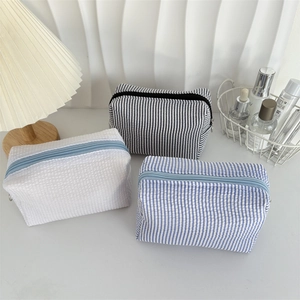 Three seersucker makeup bags in white waffle, blue and black stripes with zipper closure