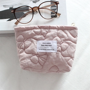 Macro view of pink quilted cotton makeup bag with bow patterns and golden zipper detail
