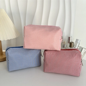 Close-up of three striped seersucker pouches with metal zippers in pink, blue and red