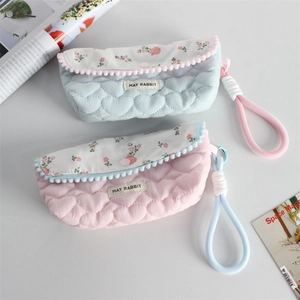 Detail of floral pencil cases showing quilted heart texture and decorative pom-pom trim