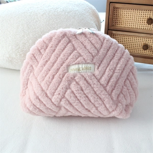 Detail of pink plush quilted makeup bag with zipper and logo in cozy setting