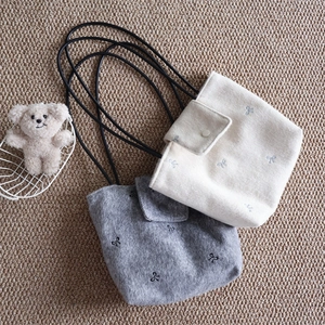 Detail of canvas tote bags with bow embroidery and cord straps on woven mat