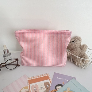Detailed shot of pink striped seersucker makeup bag with a large opening on a white desk