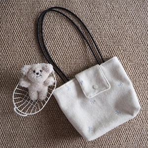 Detail of cream canvas tote bag featuring blue bow embroidery and black slim handles