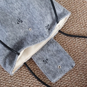 Detailed macro view of gray felt bag interior with silver snap button and bow embroidery
