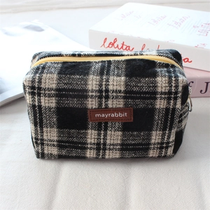 Détail de la trousse à carreaux en tweed avec zip jaune et étiquette en cuir brun