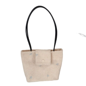 Beige canvas tote bag with blue bow embroidery and black handles on white background