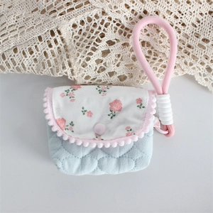 Close-up of floral fabric pouch with pink pom-poms and thick braided wrist strap