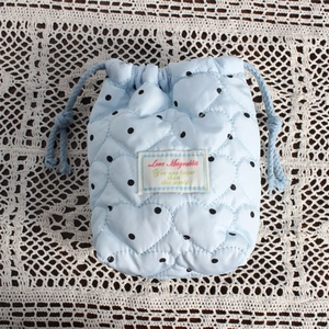 Close-up of a light blue quilted drawstring camera bag with black dots and heart patterns