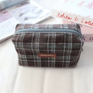 Détail de la trousse à maquillage en laine à carreaux avec étiquette en cuir et zip métal