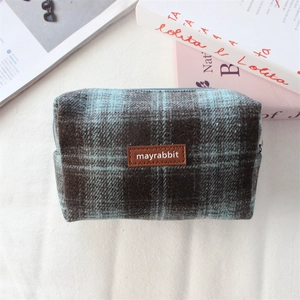 Gros plan d'une trousse à maquillage à carreaux avec logo en cuir et texture en laine