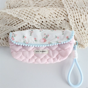 Detail of pink floral quilted pouch with soft heart texture and blue pompom trim