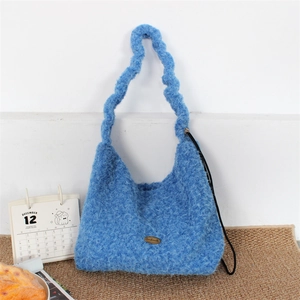 Close-up of blue fuzzy plush tote bag showing handmade metal tag and wavy strap detail