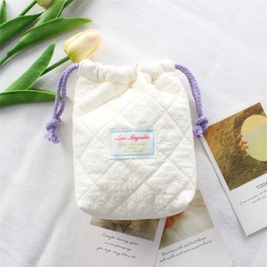 Close-up of quilted white cotton camera bag with purple drawstrings and embroidered logo