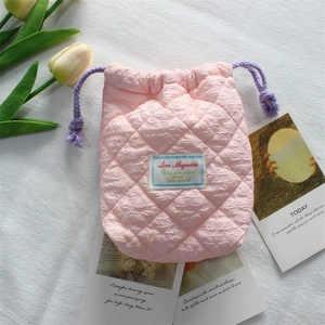 Detailed view of quilted pink camera pouch with drawstring and logo label on white cloth