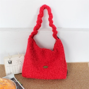 Close-up of red plush tote bag with wavy padded handle and handmade metal logo