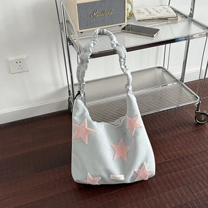 Blue canvas shoulder bag with pink plush stars and ruffled strap on wood floor