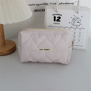Close-up of pink quilted cosmetic bag with heart embroidery and brand logo label