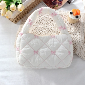 Detailed close-up of quilted white handbag with pink bow embroidery and soft fabric texture