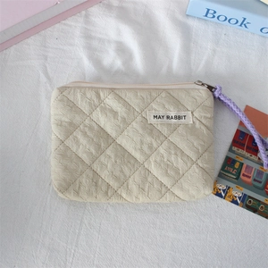 Detail of beige quilted coin purse with purple woven zipper pull and branded label