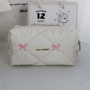 Detail of white quilted makeup bag with pink bow embroidery and metal zipper closure