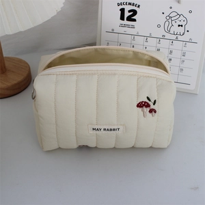 Detailed view of cream quilted makeup bag with red mushroom embroidery and soft texture