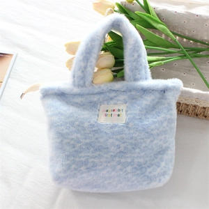 Detailed close-up of soft ice blue plush handbag with a white woven label and short handles