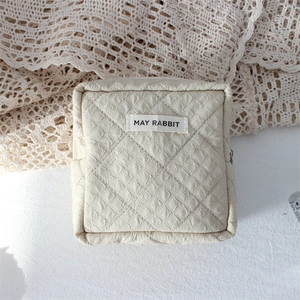 Detailed close-up of a quilted cream makeup bag with May Rabbit label on a lace fabric