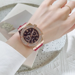 Close-up of rose gold quartz watch with rhinestone bezel and red silicone strap on wrist