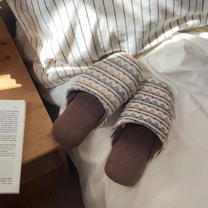 Nahaufnahme von Leinenpantoffeln mit Boho-Muster auf einem gemütlichen weißen Bett