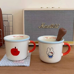 Close-up of ceramic mugs featuring Hello Kitty apple patterns and red U-shaped handles