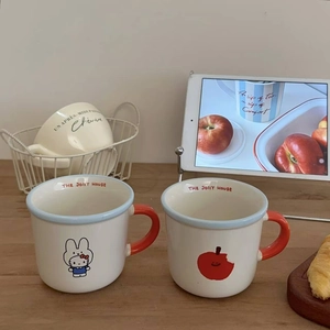 Detail of cream ceramic mugs featuring cute bunny and apple patterns with red handles