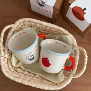 Close-up of a ceramic mug set with cat and apple motifs inside a woven basket