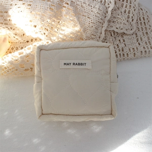 Close-up of heart-shaped quilted pattern and woven label on cream cosmetic bag