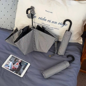Detail of folding gingham umbrella with vintage black hooked handle on bed