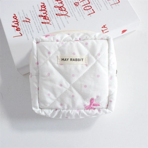 Detail of white quilted cosmetic pouch with pink dots and embroidered bow decoration