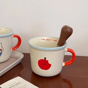 Detail of ceramic mug with red apple pattern, blue rim and wooden stirring spoon