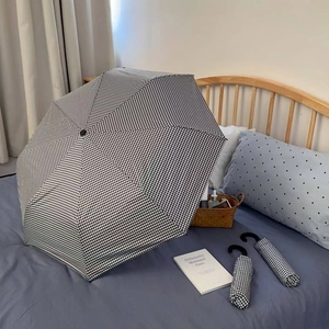Detail of checkered sun umbrella with vintage J-shaped handle on a cozy bed background