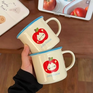 Close-up of stacked ceramic mugs with cute apple cat pattern and blue rims on wood desk