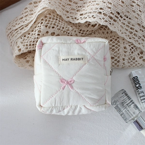 Detailed view of quilted white cosmetic bag with pink bow embroidery and branded label