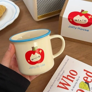 Close-up of cream ceramic mug featuring cute cat apple illustration and blue rim detail