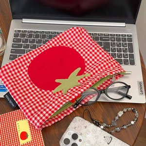 Detail der rot-weiß karierten Tomaten-Kosmetiktasche auf einem Laptop mit Accessoires