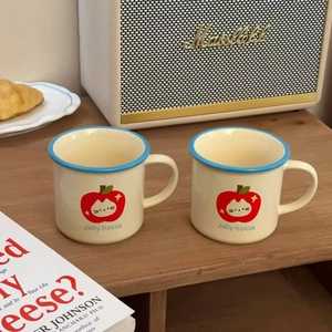 Detail of two cream ceramic mugs with cute cat and apple prints on a wooden table