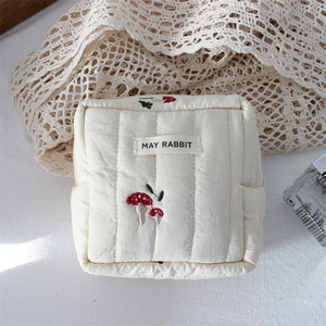 Detail view of cream quilted makeup bag featuring mushroom embroidery and brand label