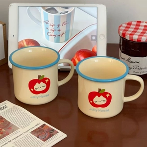 Detail of two cute ceramic mugs with red apple cat prints on a cozy tea table setting